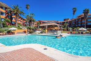 Ein Hotelpool mit klarem, blauem Wasser, Palmen und Sitzmöglichkeiten im Freien.