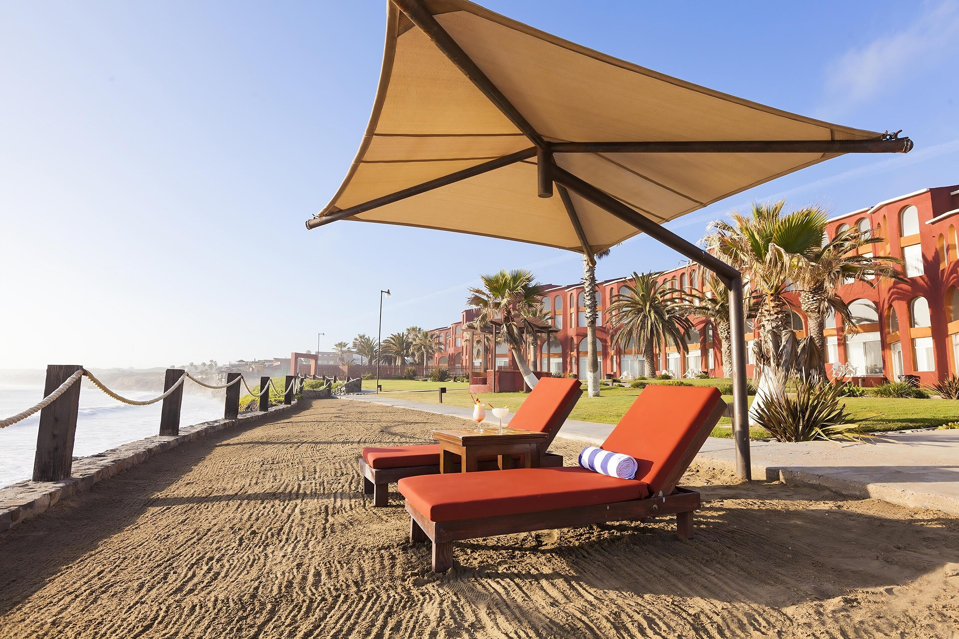 A beachside lounge area with sun loungers, a large umbrella, and a view of the ocean.