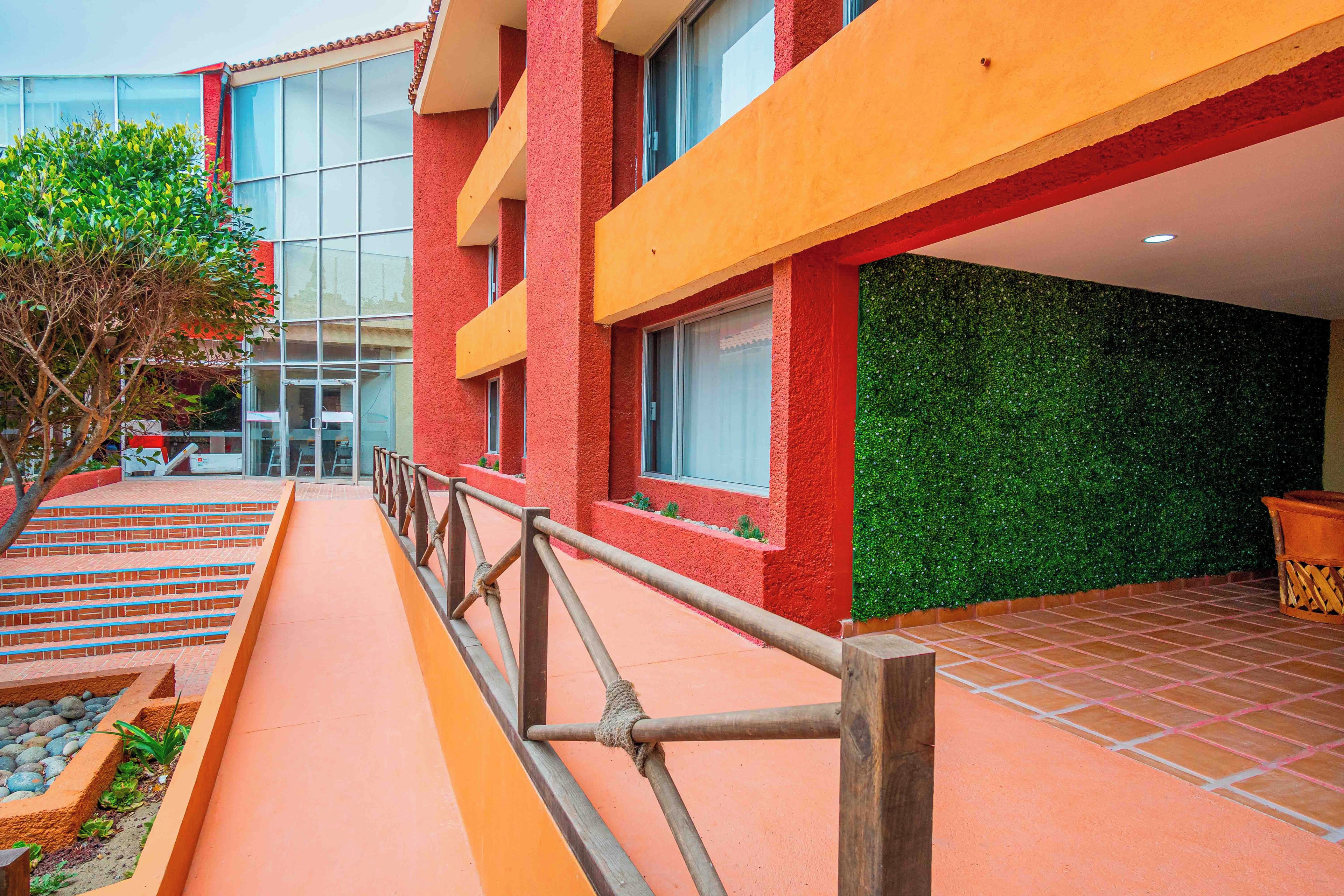 A building with a red exterior, a glass entrance, and a green wall. There are steps leading to the entrance and a railing in the foreground.