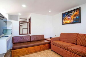 Una sala de estar moderna con un sofá de cuero marrón, un sofá naranja con estampado, un cuadro en la pared y una estantería empotrada.