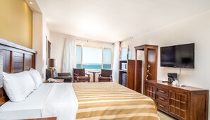 Ein Hotelzimmer mit einem großen Bett, einem Fernseher, einem Schreibtisch mit Stuhl und Blick aufs Meer.