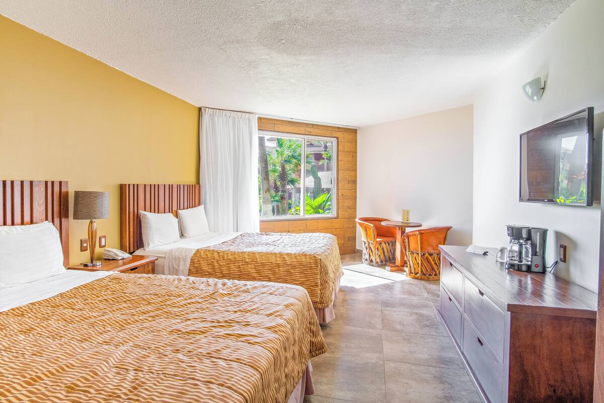 A hotel room with two beds, a desk, a chair, a coffee maker, and a TV.