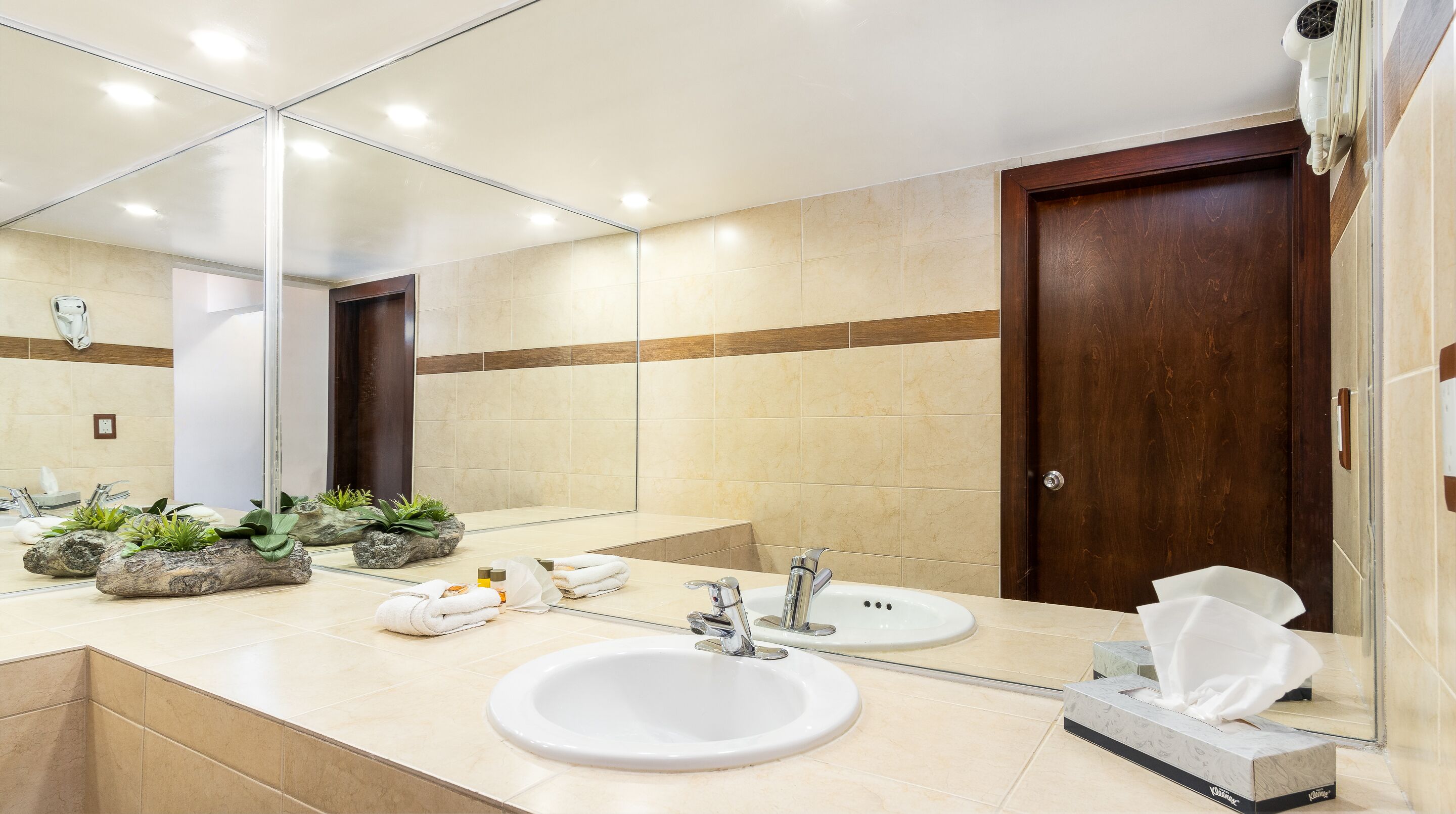 Un baño moderno con dos lavamanos, un espejo grande y una puerta de madera.
