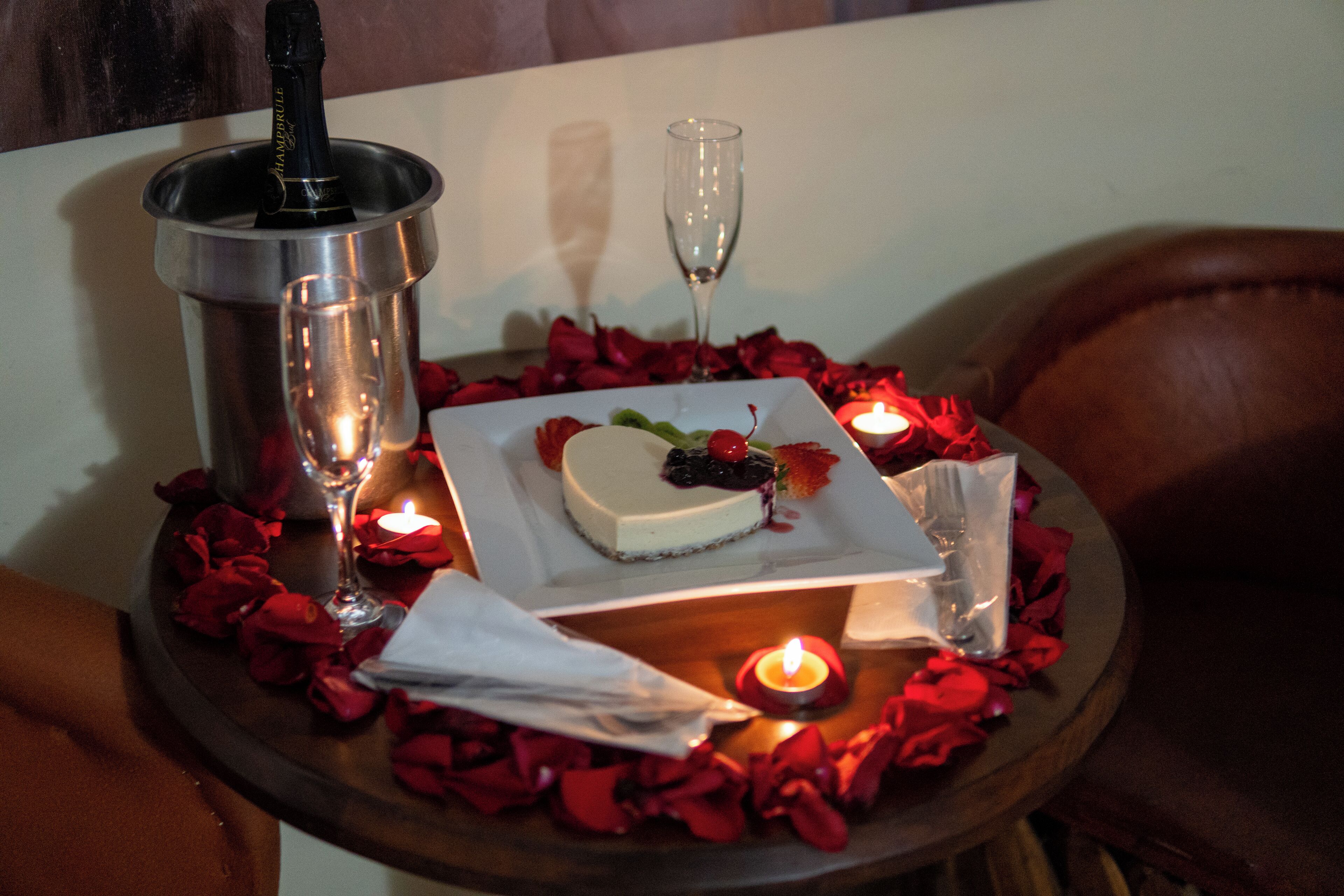 Una mesa con un pastel con forma de corazón, una botella de champán y velas.