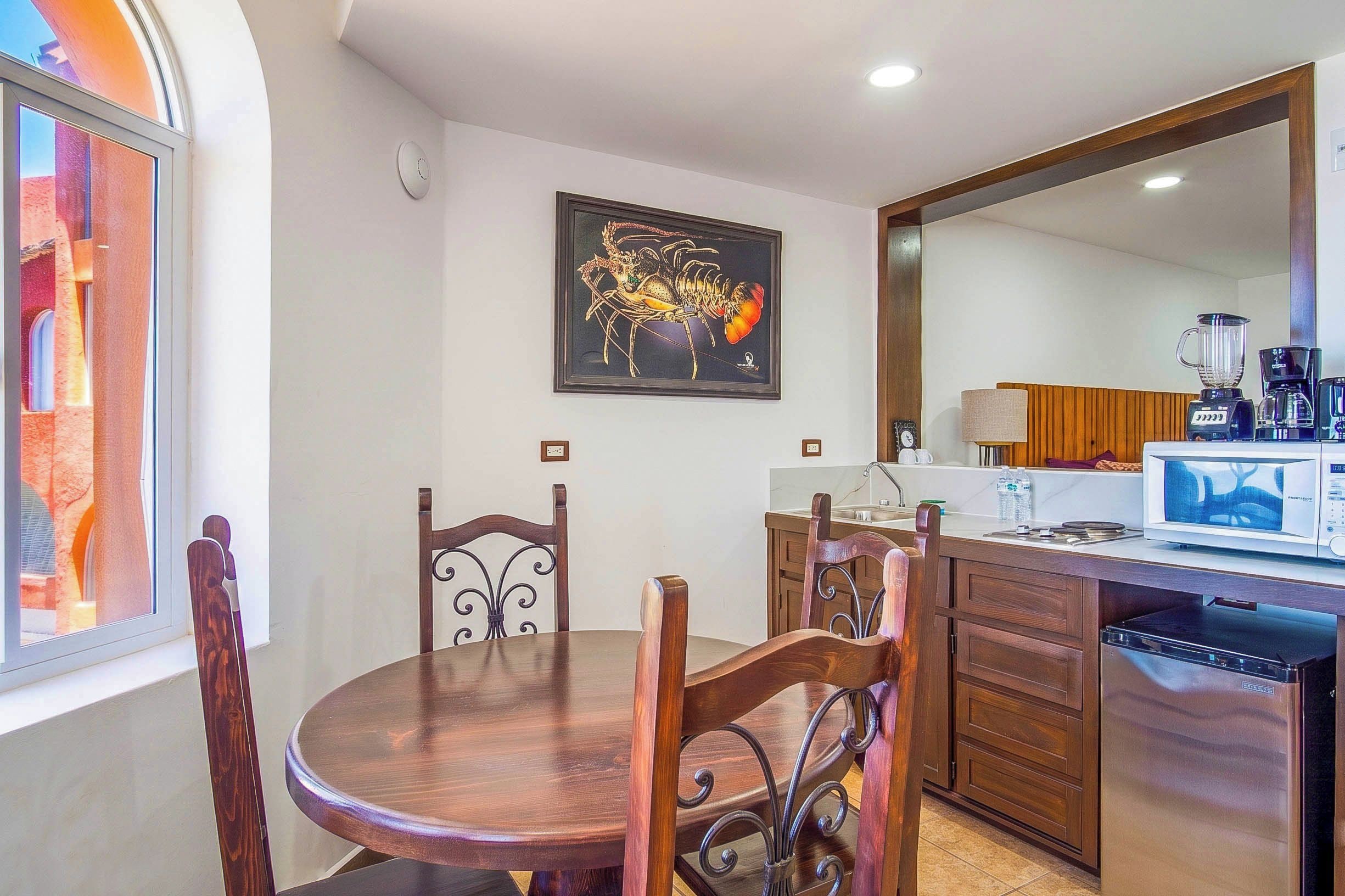 Un comedor con una mesa redonda y sillas, una cocina con microondas, y una obra de arte enmarcada en la pared.