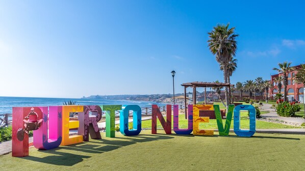 Ein farbiges Schild mit der Aufschrift "PERTO NUEVO" im Hintergrund mit Blick auf die Küste.