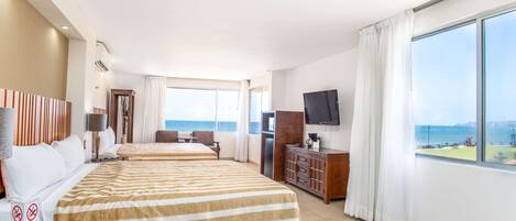 Quarto de hotel com duas camas, televisão, secretária e vista para o mar.