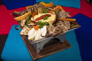 Ein Servierteller aus Metall mit gegrilltem Fleisch, Gemüse und Käse auf einer Holzplatte.
