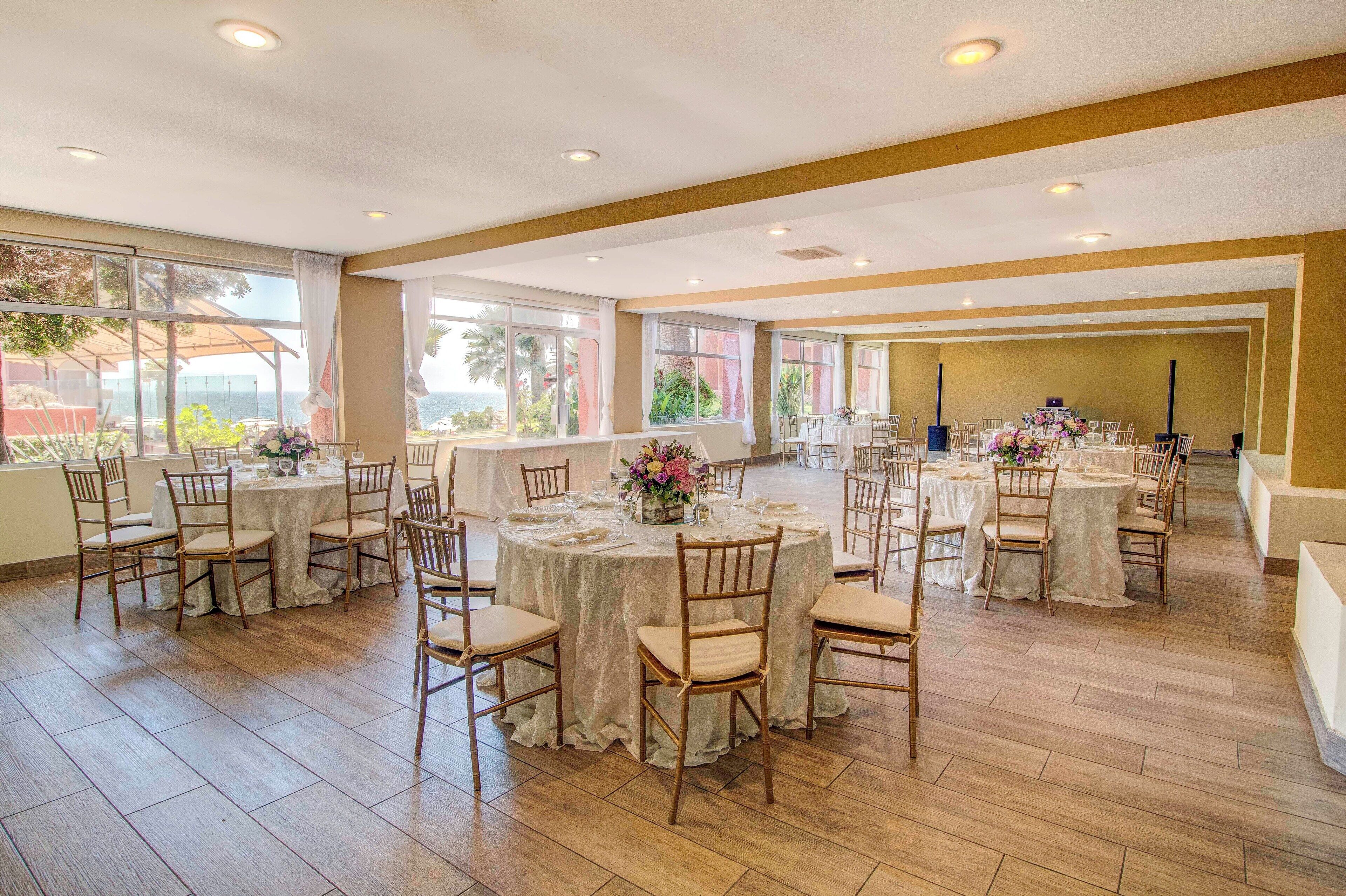 A spacious banquet hall with multiple round tables, each set with white tablecloths and floral centerpieces.