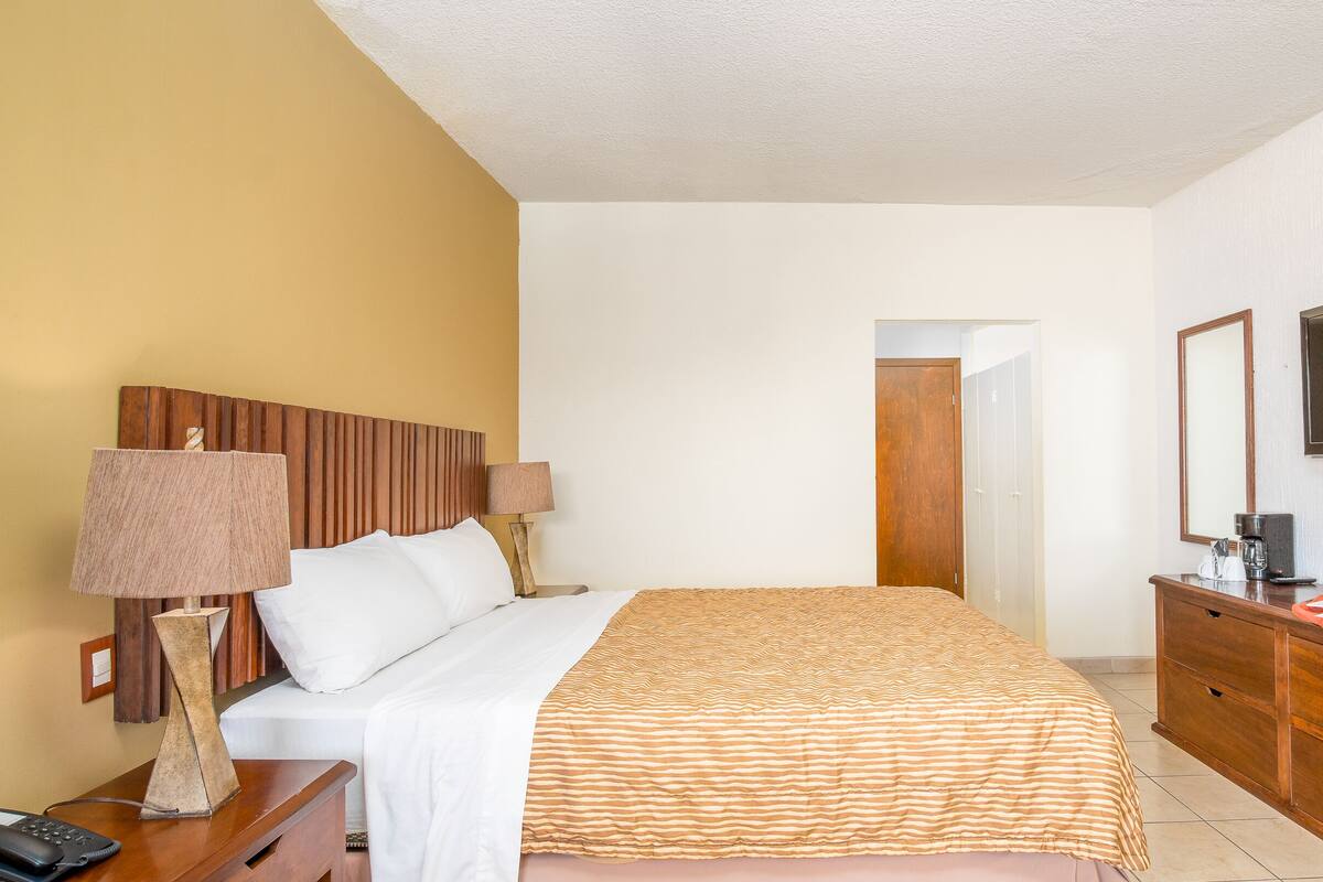 A hotel room with a bed, bedside lamps, a dresser, a television, and a breakfast tray.