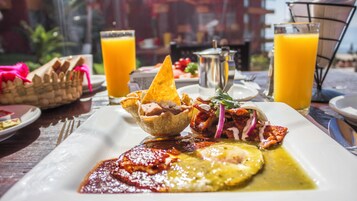 A meal with a tortilla bowl, a plate with a red sauce, and two glasses of orange juice on a wooden table.