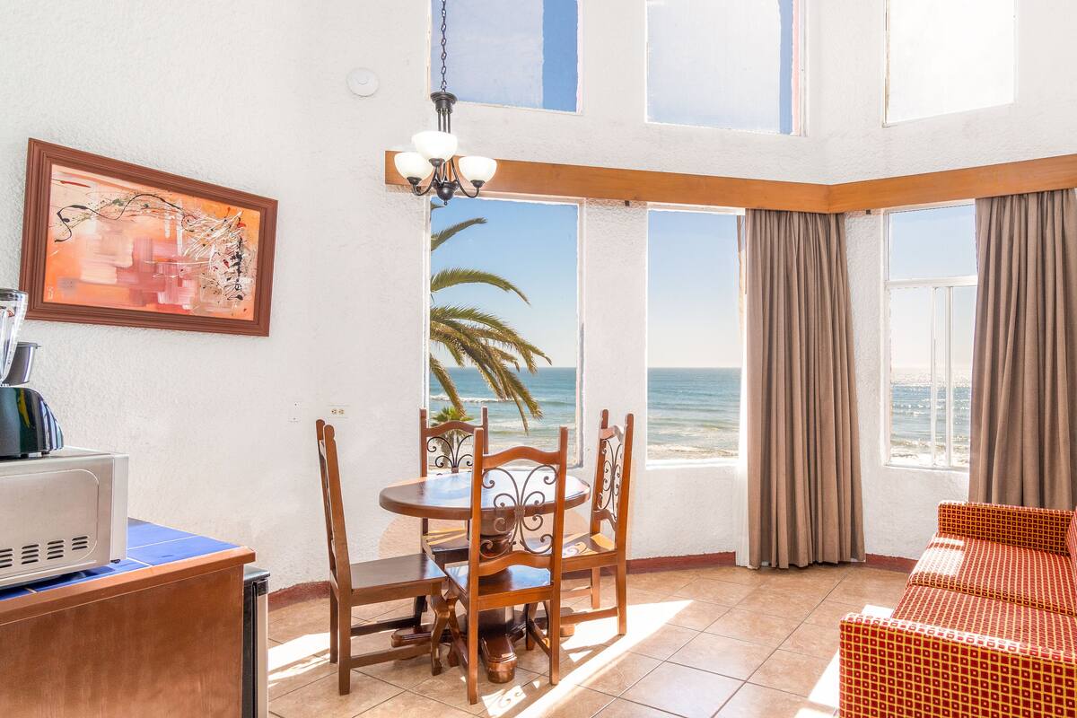 A room with a dining table and chairs, a sofa, a painting, and a view of the ocean.