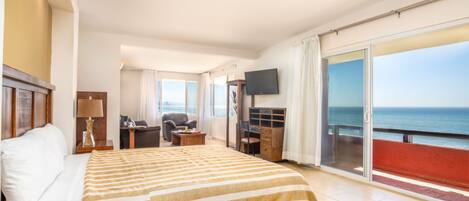Habitación de hotel con una cama grande, un escritorio, una silla, un televisor y un balcón con vistas al mar.