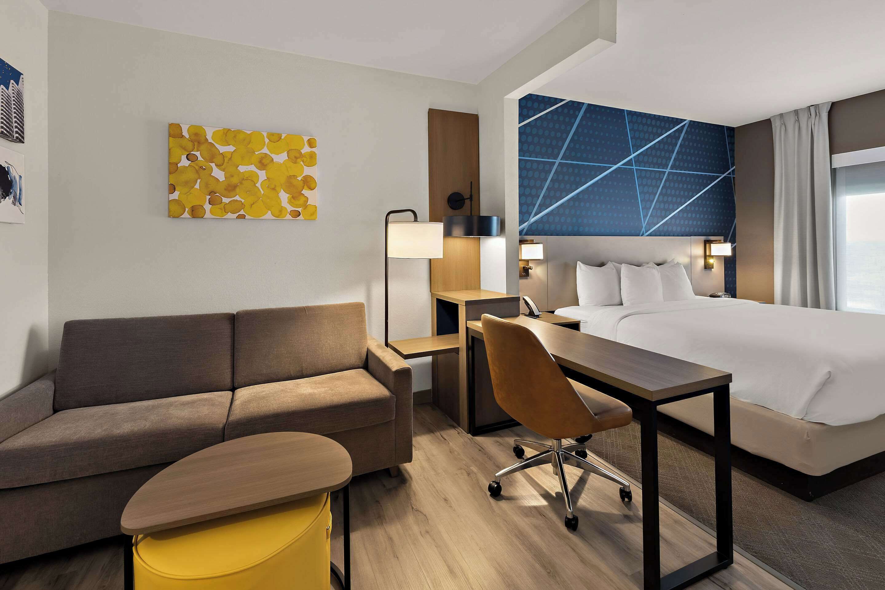 Une chambre d’hôtel moderne équipée d’un canapé, d’un bureau, d’une chaise, d’un lit et d’une grande fenêtre.