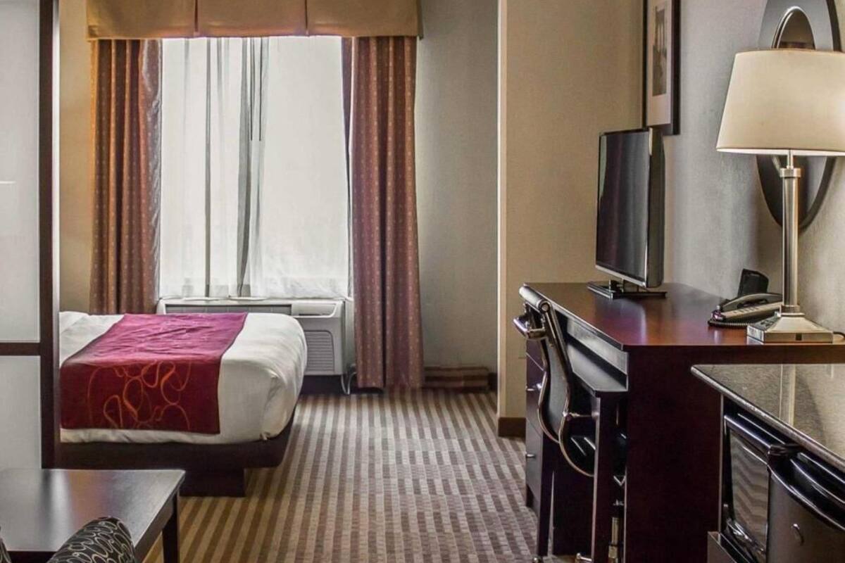 A hotel room with a bed, a desk with a TV, a lamp, and a window with curtains.