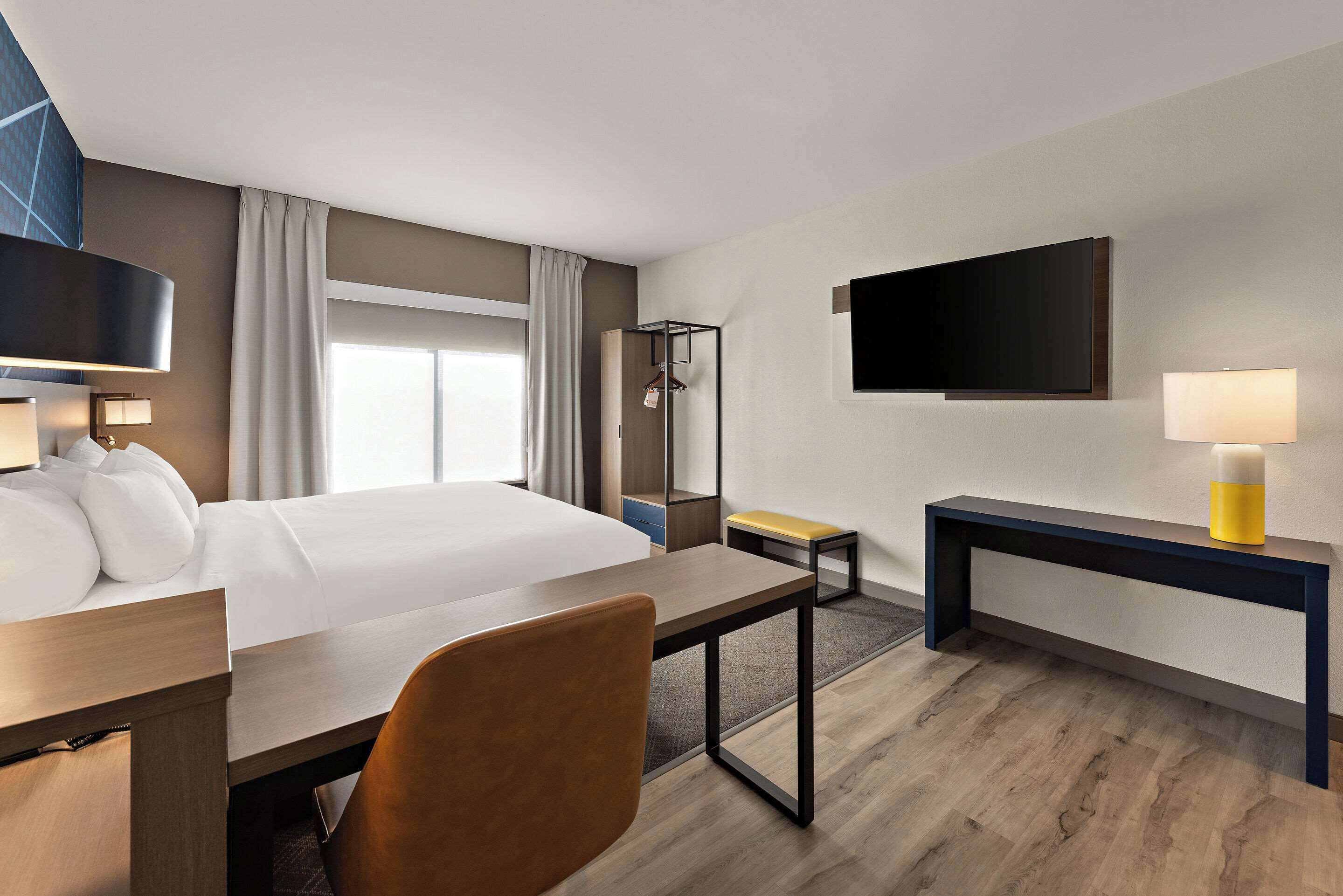 Ein Hotelzimmer mit Bett, Schreibtisch, Stuhl, Nachttisch, Fernseher und Kleiderhaken.