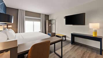 Ein Hotelzimmer mit Bett, Schreibtisch, Stuhl, Nachttisch, Fernseher und Kleiderhaken.