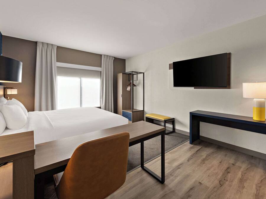 Ein Hotelzimmer mit Bett, Schreibtisch, Stuhl, Nachttisch, Fernseher und Kleiderhaken.