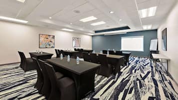 Uma sala de conferências com mesas, cadeiras e um projetor.