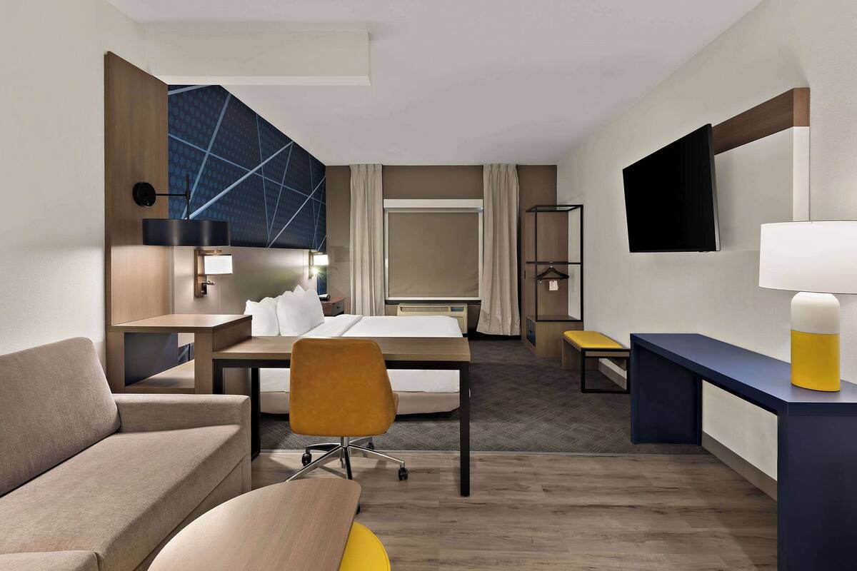 A hotel room with a bed, a sofa, a desk, a chair, a TV, and a bedside table.