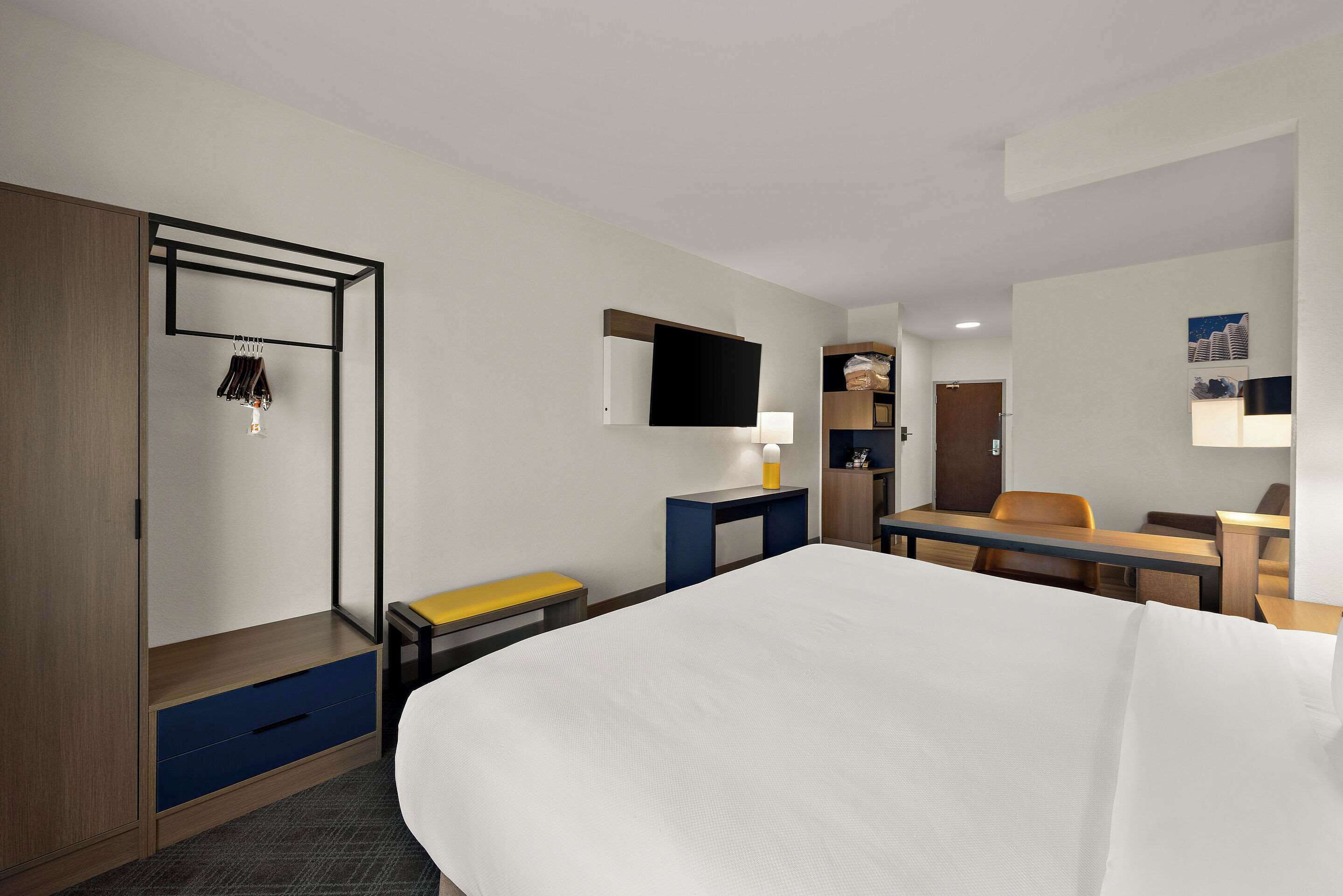 Ein Hotelzimmer mit Bett, Schreibtisch, Stuhl, Kleiderschrank und einem Fernseher an der Wand.