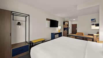 Ein Hotelzimmer mit Bett, Schreibtisch, Stuhl, Kleiderschrank und einem Fernseher an der Wand.
