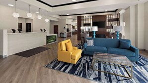 A modern hotel lobby with a reception desk, a yellow armchair, a blue sofa, and a patterned rug. - Comfort Suites Columbus East Broad (Columbus)