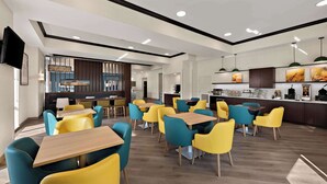 A modern hotel lobby with a dining area featuring yellow and teal chairs, wooden tables, and a central bar area. - Comfort Suites Columbus East Broad (Columbus)