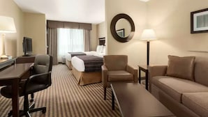 A hotel room with a bed, two chairs, a desk, a TV, a lamp, and a large mirror. - University Hotel - Davis Area by IHG (Dixon)