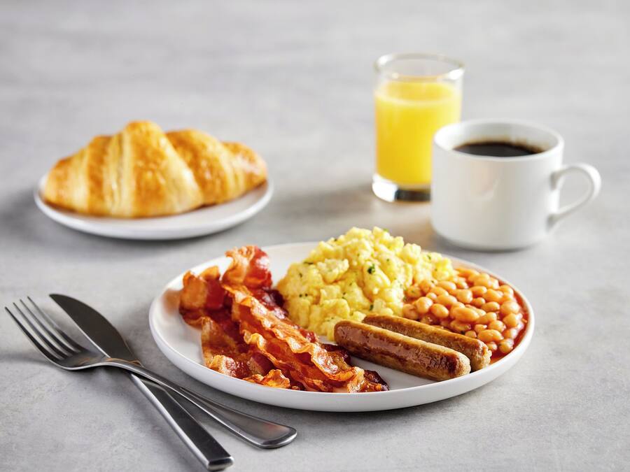 Prato de café da manhã com ovos, feijão, bacon e um croissant sobre uma mesa.