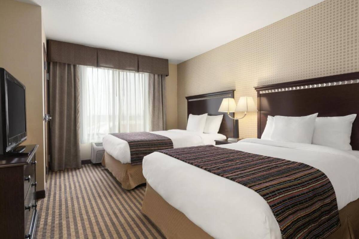 Habitación de hotel con dos camas, televisor y un amplio ventanal con cortinas.