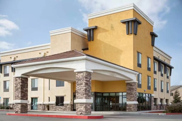 A hotel with a yellow facade, a covered entrance, and stone pillars. - University Hotel - Davis Area by IHG (Dixon)