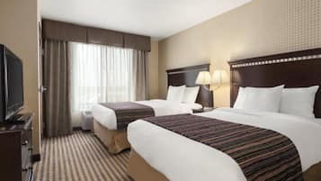 Habitación de hotel con dos camas, televisor y un amplio ventanal con cortinas.