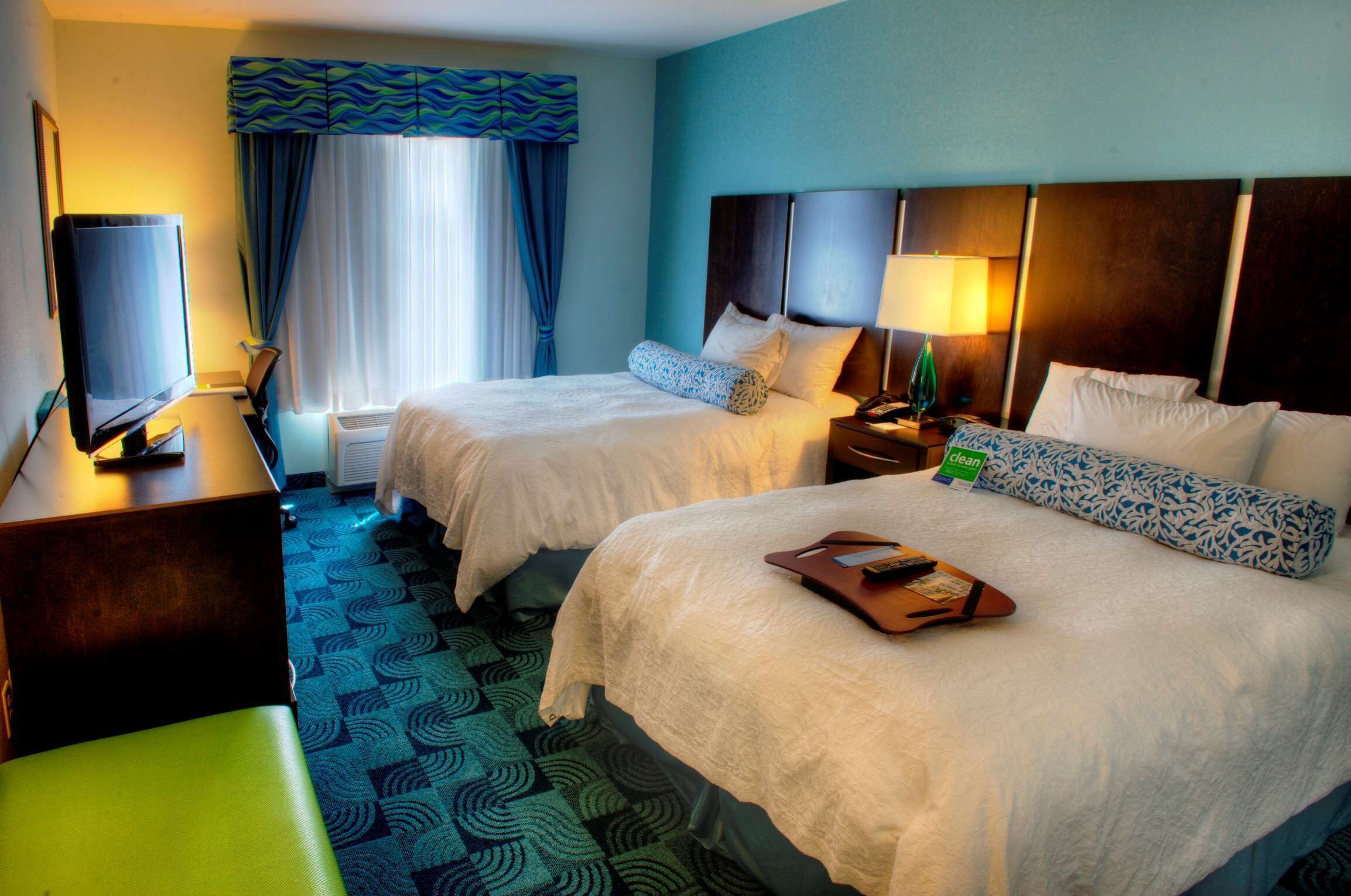 A hotel room with two beds, a desk with a television, a chair, and a bathroom with a shower and toilet.