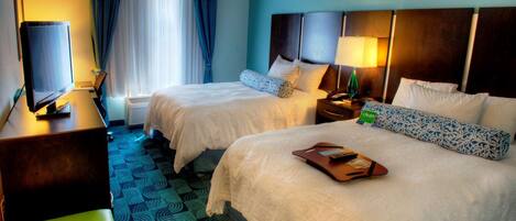 A hotel room with two beds, a desk with a television, a chair, and a bathroom with a shower and toilet.