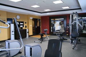 Un gimnasio con máquinas de cardio, equipo de entrenamiento con pesas y un espejo.