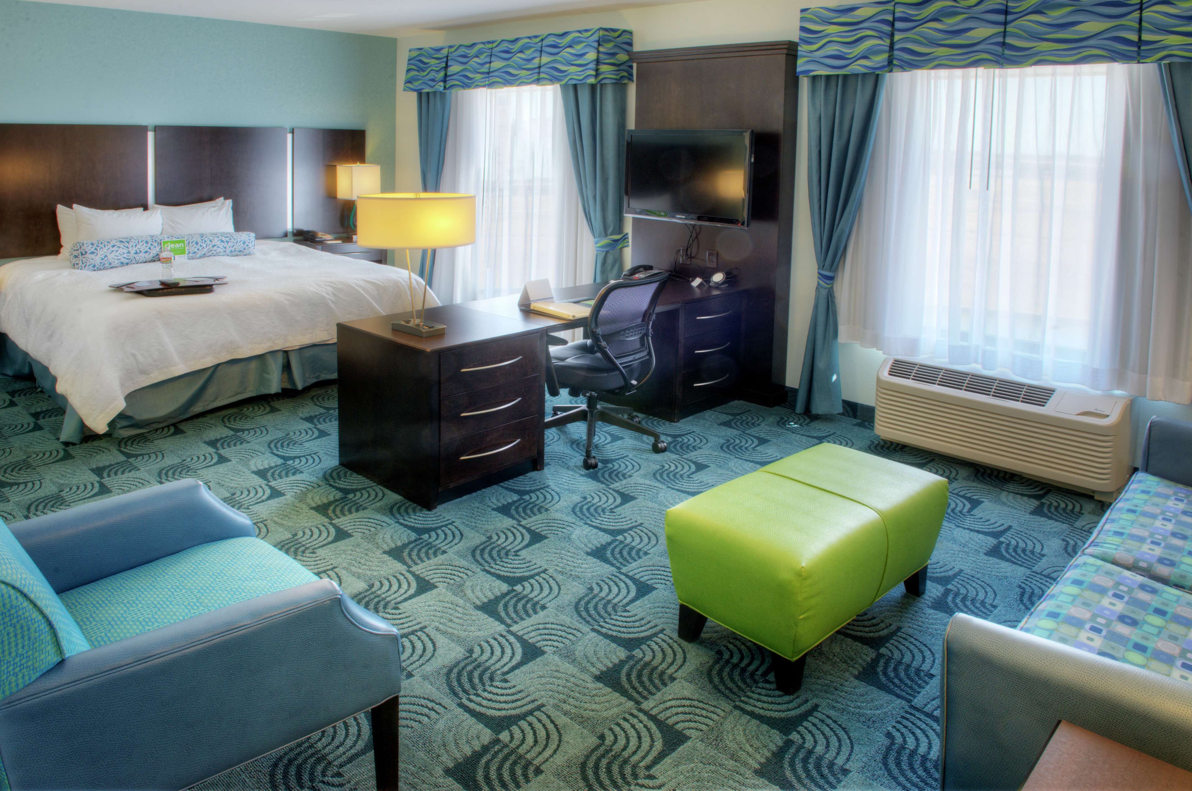 A hotel room with a bed, desk, chair, and an ottoman.