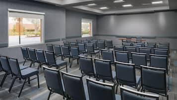 A conference room with rows of chairs, large windows, and a carpeted floor.