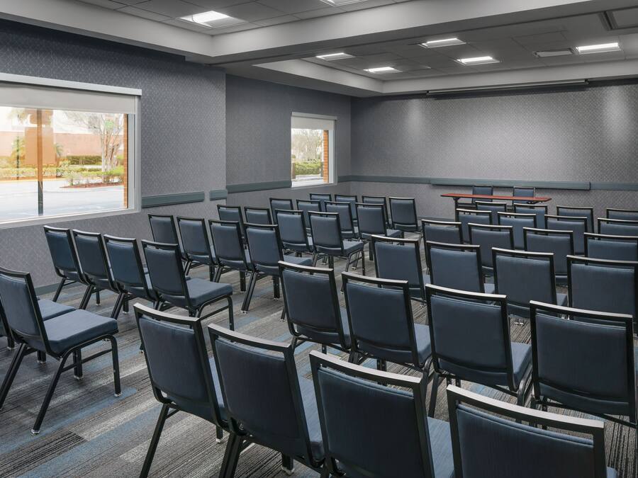 A conference room with rows of chairs, large windows, and a carpeted floor.