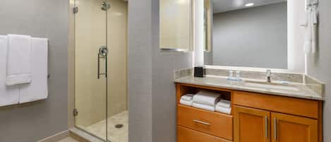 Un baño moderno con ducha de vidrio, un espejo grande y armarios de madera.