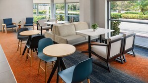 A modern indoor seating area with tables and chairs, large windows, and a view of greenery outside.