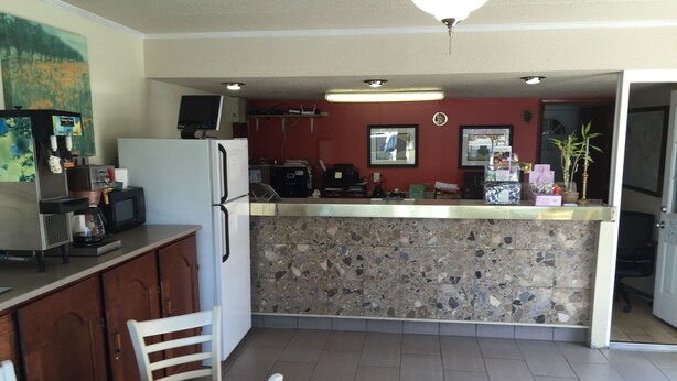 A kitchen with a stone backsplash, a refrigerator, a microwave, and a coffee maker. There is a table with a Dunkin' Donuts box on it. - Kings Inn (Lenoir City)
