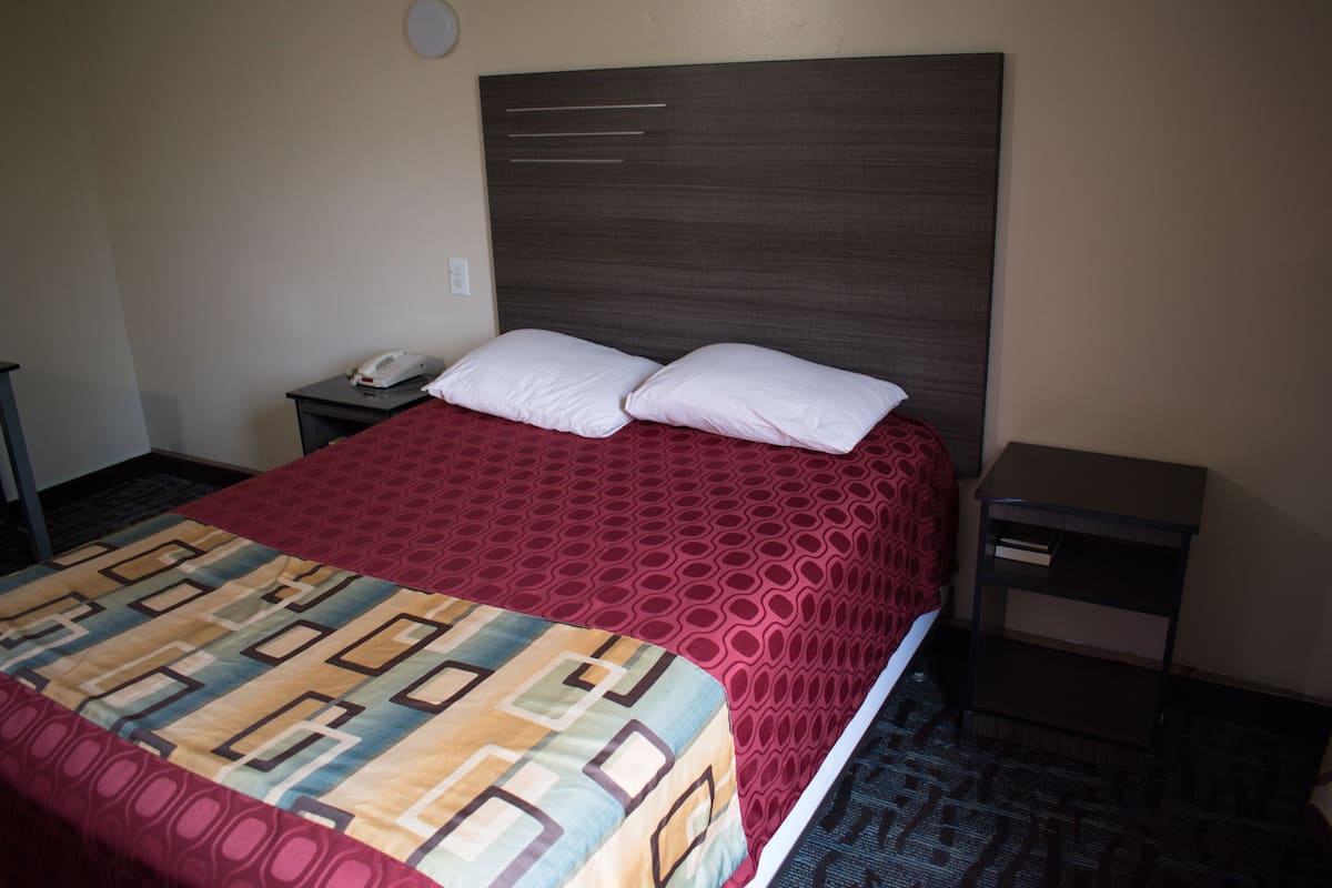 A hotel room with a large bed, two pillows, a bedside table with a phone, and a nightstand.