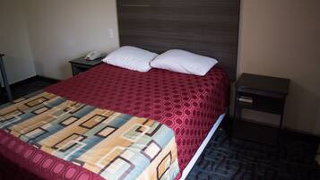 Habitación de hotel con una cama grande, dos almohadas, una mesita de noche con un teléfono y una mesita auxiliar.