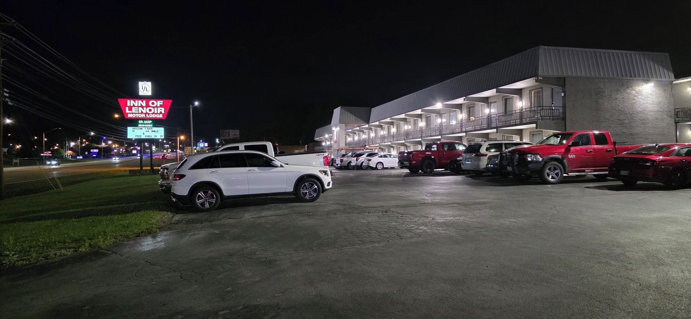 A motel with a row of rooms, a parking lot with several cars, and a sign for the Inn of Lenoir Motor Lodge.