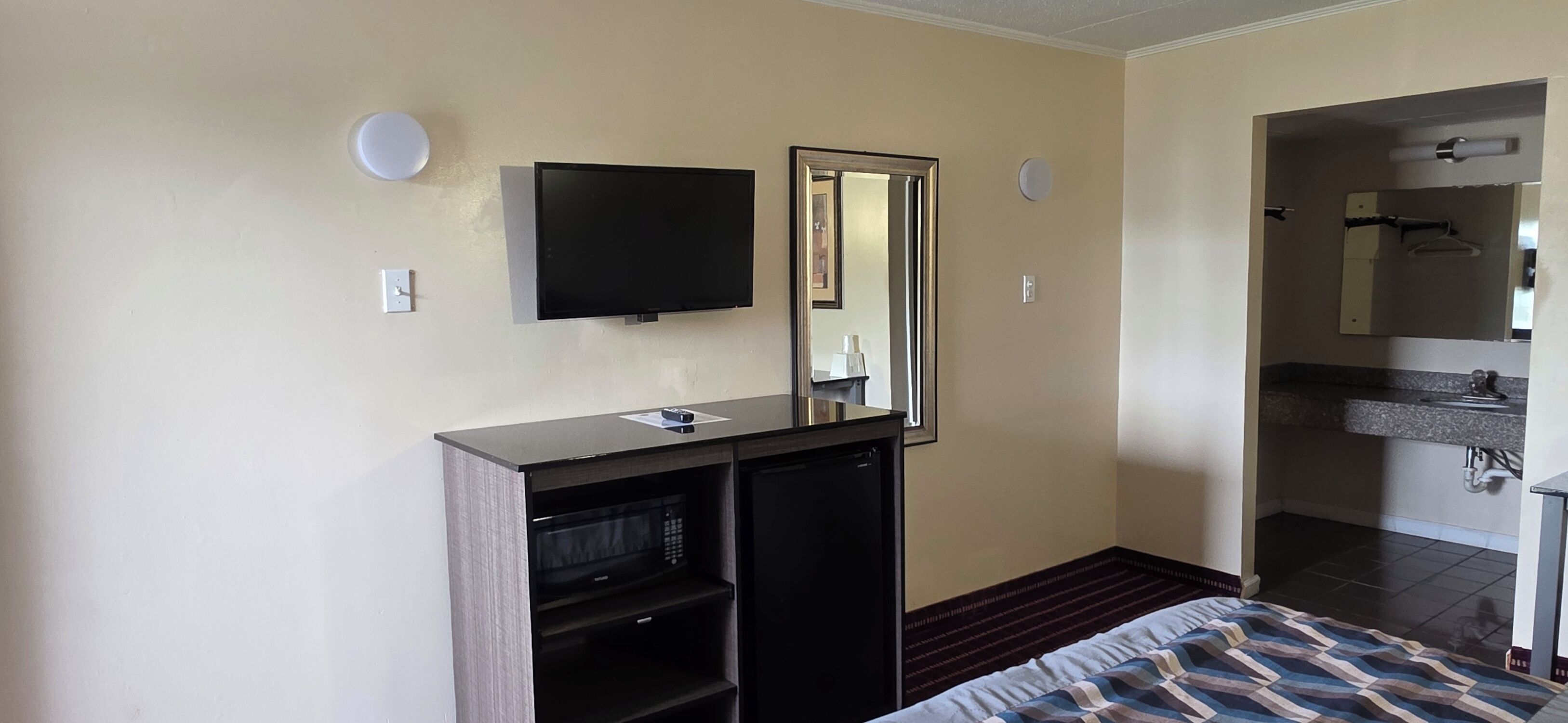 Una camera d'albergo con un letto, una TV, uno specchio, un angolo cottura e un bagno.