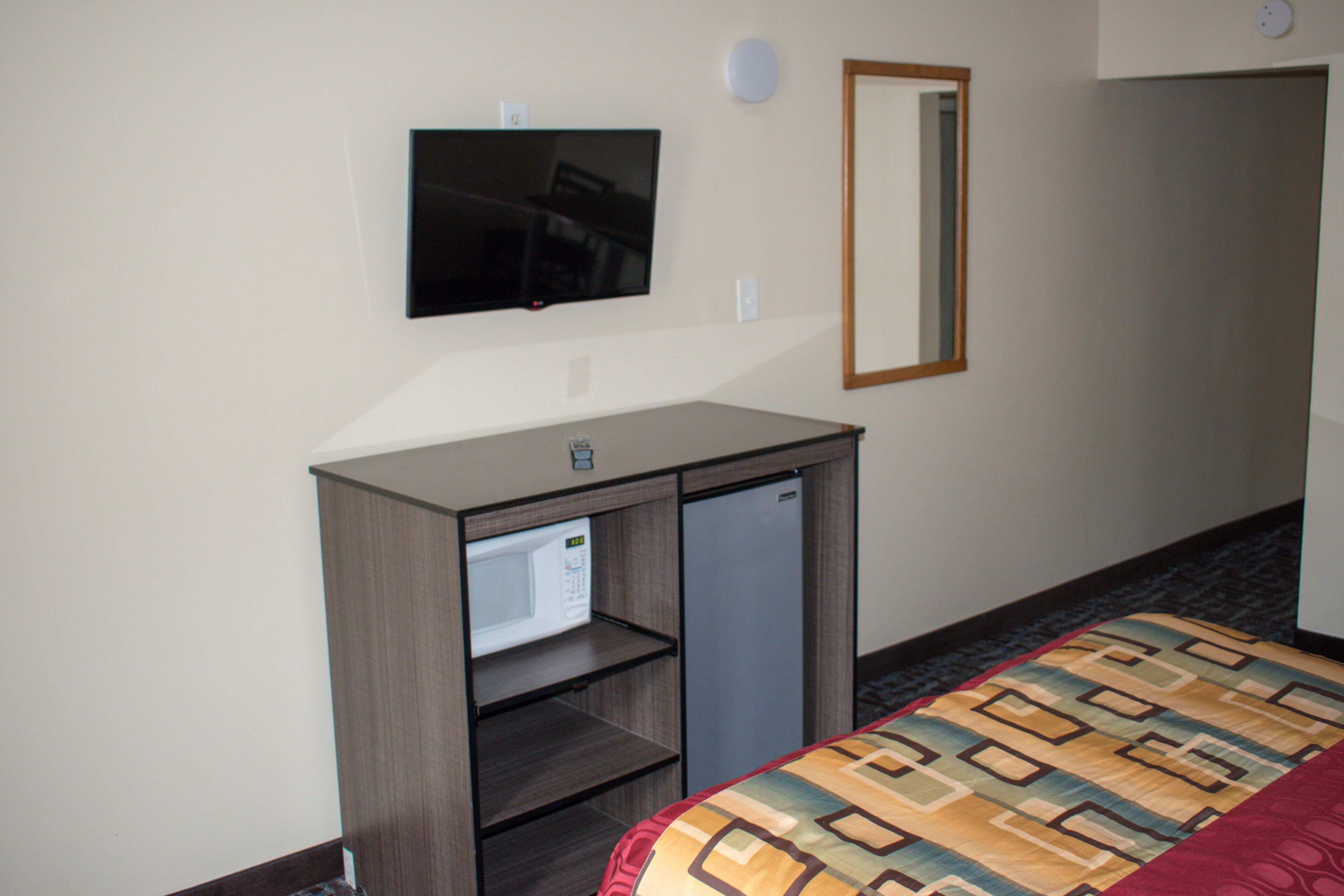 A hotel room with a bed, a TV mounted on the wall, a microwave, and a refrigerator.