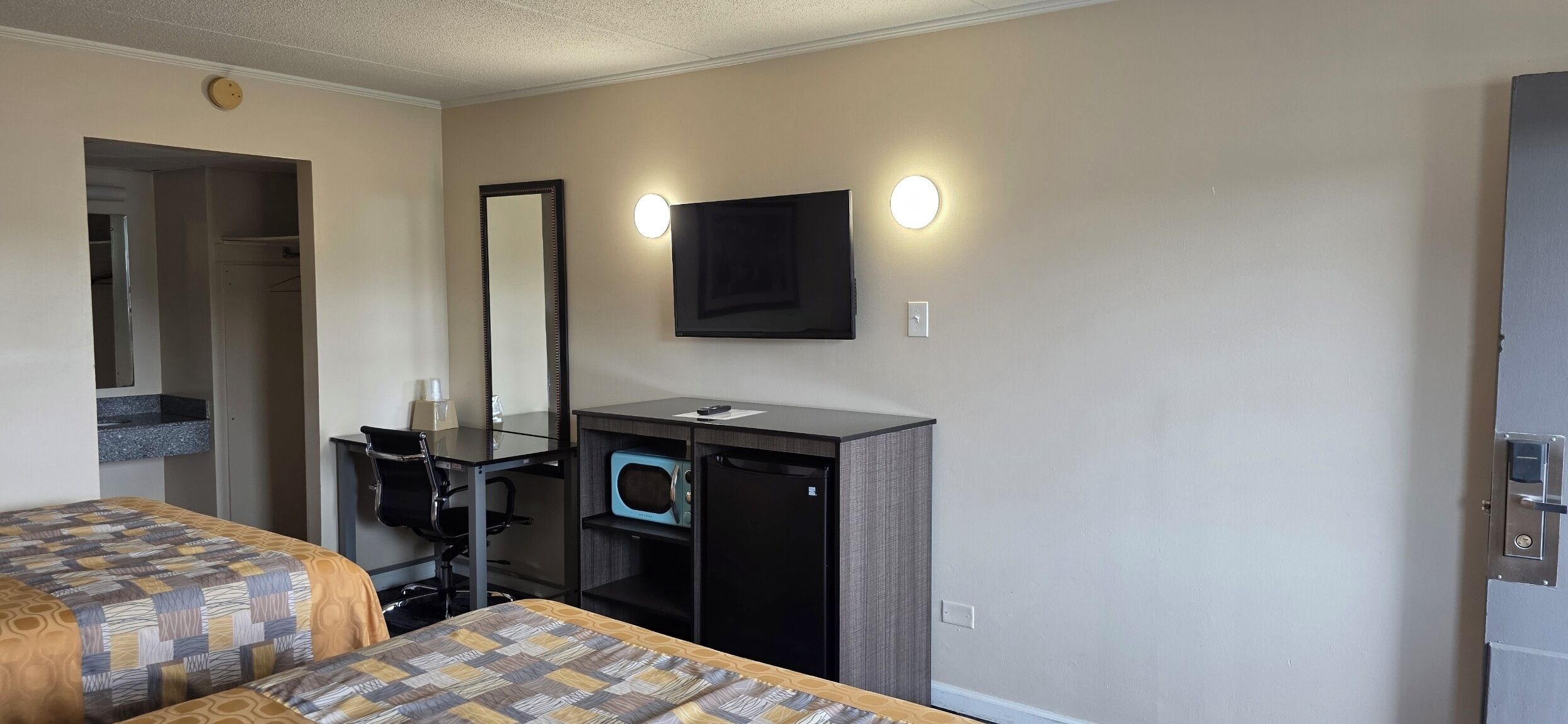 Habitación de hotel con dos camas, un escritorio con espejo, televisor de pantalla plana, microondas y un mueble pequeño.