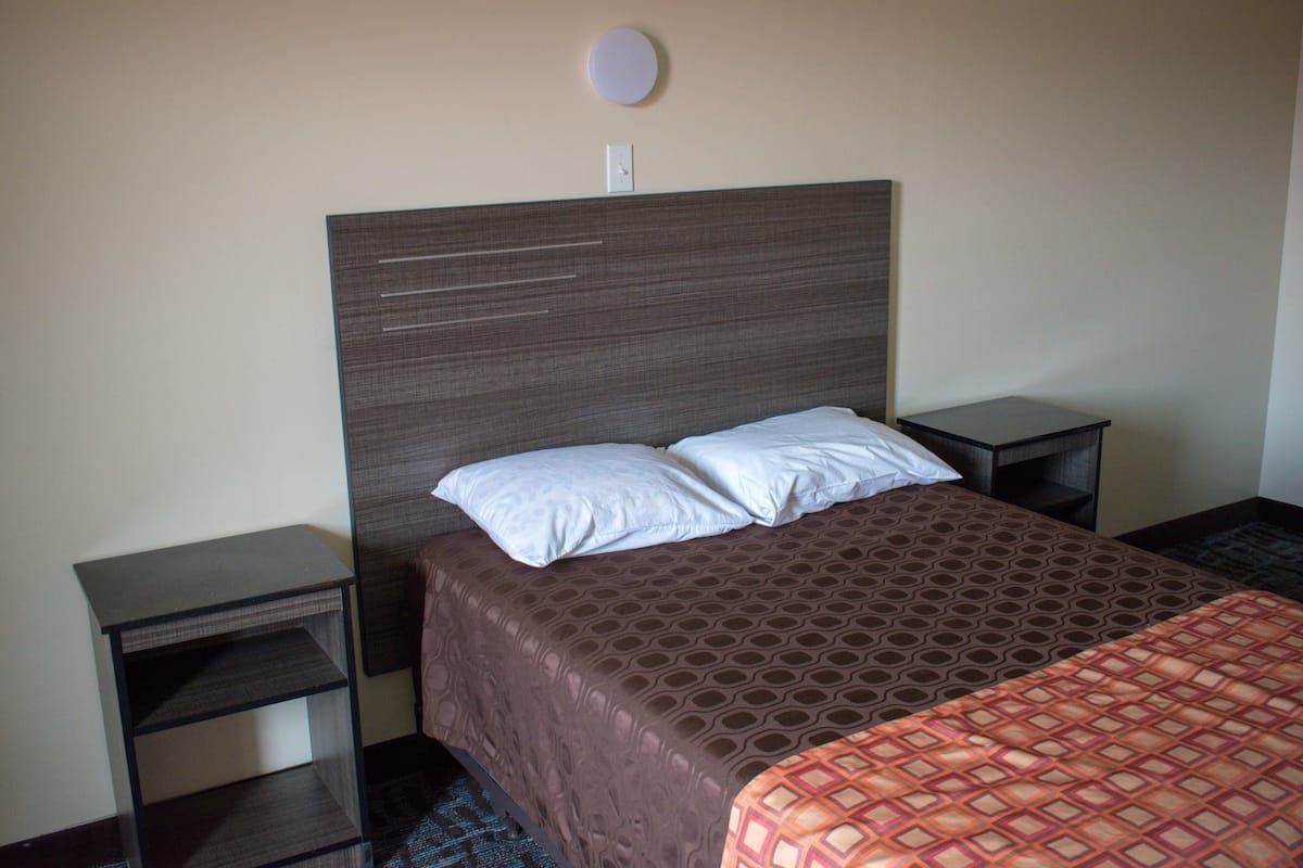 A hotel room with a large bed, two bedside tables, and a wall-mounted light fixture.