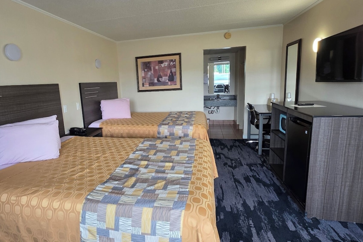 A hotel room with two beds, a desk, a television, and a bathroom visible through an open door.